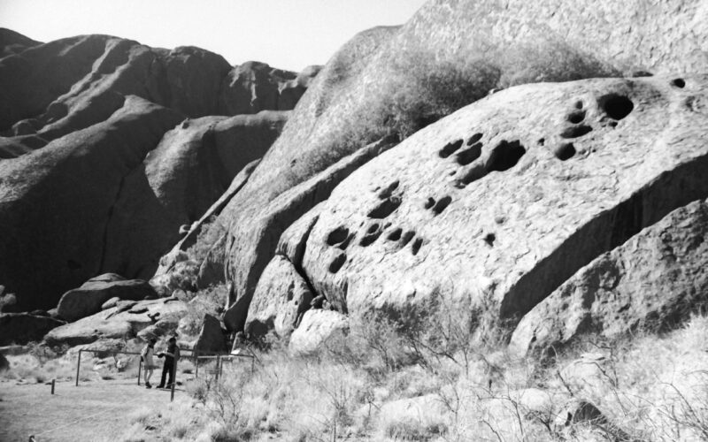 Black and white photograph of Uluru with two people standing to the side