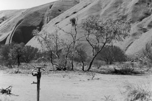 Black and white photograph of Uluru with a water tap in the foreground