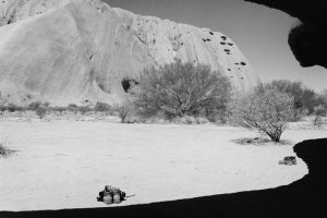 Black and white photograph of Uluru with two pairs of boots in the foreground