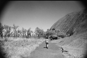Black and white photograph of Uluru with two people walking along a path