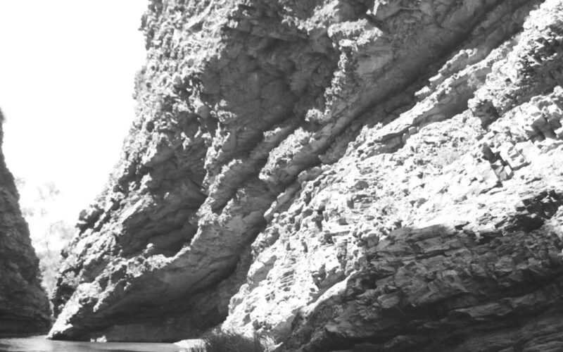 Black and white photograph of a large rock face with a small water pool beneath it