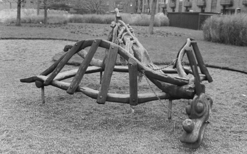 Black and white photo of a wooden playground climbing structure in the shape of a dragon.