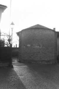 Black and white photo of the side of a round stone building with a paved road in front of it.