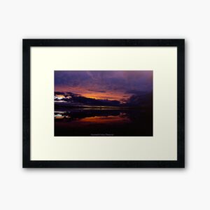 Photography framed in a black frame with a large white border. The photo is of a sunset over a salt lake with the pink and orange of the sky and the lake reflected. It is signed Frogmouth Cottage Photography.