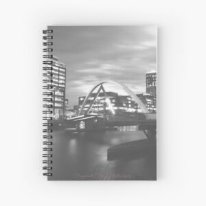 Spiral notebook with a black and white image of a city scape at night with a curved briedge across a river in the foreground. It is signed by Frogmouth Cottage Photography.