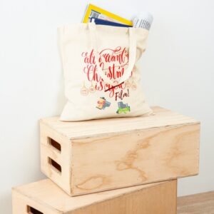 Photo of a canvas bag sitting on wooden boxes. The bag is filled with magazines and newspapers. The print on the bag says "All I want for Christmas is Film! and has christmas baubles and gifts of film and cameras.