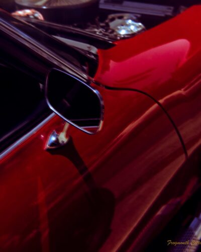 Close up photo of the side door and mirror of ared car. The shining metal of the engine is just visible as the bonnet is up