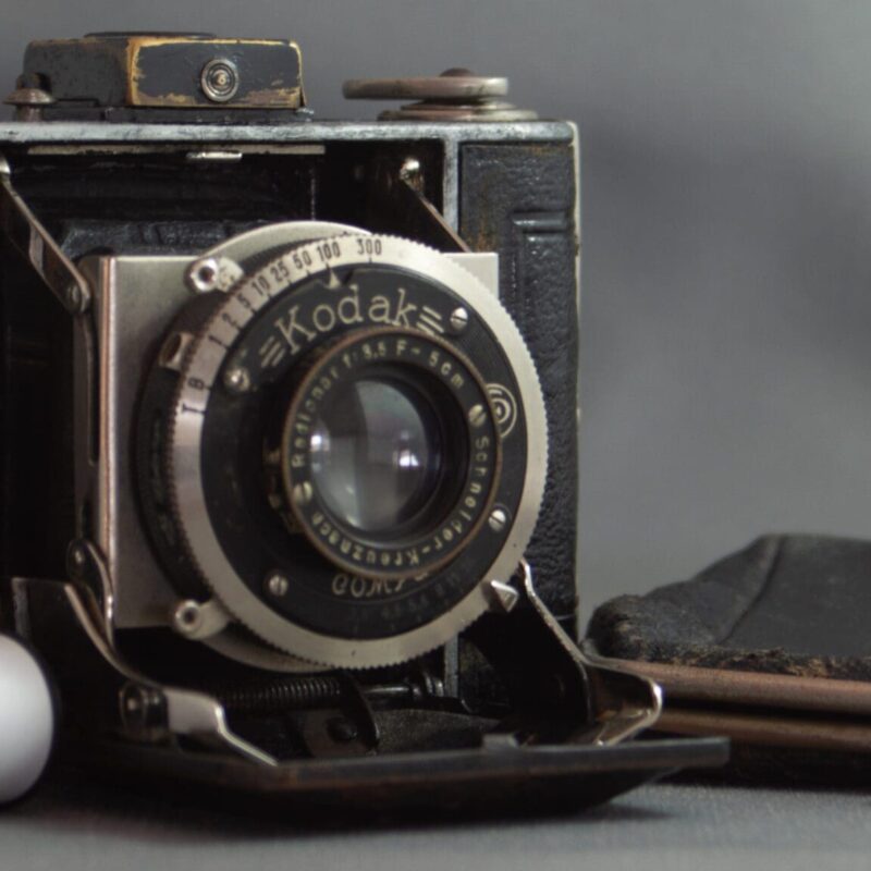 Photograph of a Kodak Vollenda 48 camera - a folding 127 roll film camera. The camera is open with the bellows folded out. There are two rolls of 127 film on the left hand side and a small purse (that the camera fits into) on the other side.