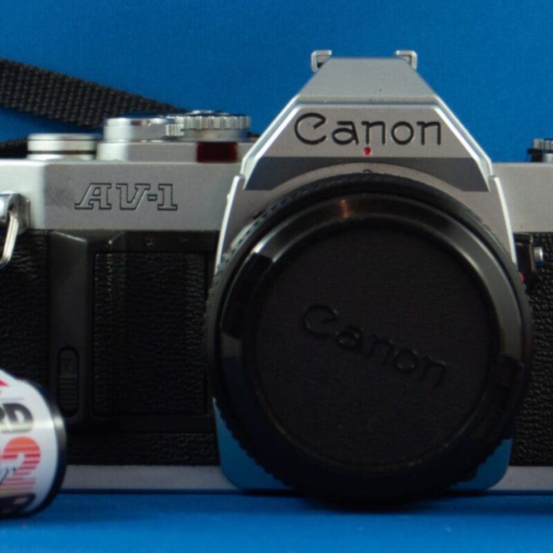 Photograph of a Canon AV-1 SLR camera with a strap and three rolls of film.