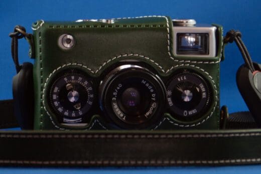 Photograph of a Rollei 35 camera in a green leather case with a matching neck strap lying around it.