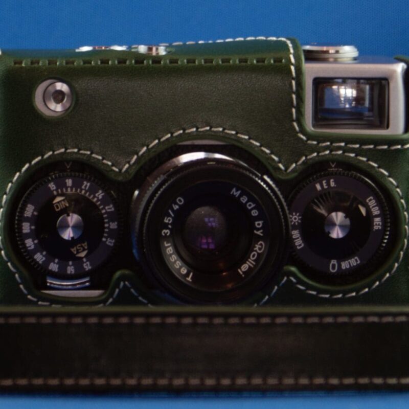 Photograph of a Rollei 35 camera in a green leather case with a matching neck strap lying around it.