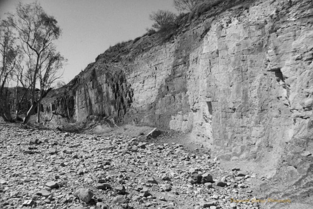 Black and white photo of a wall of ochre in different shades, carved out by indigenous peoples
