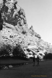 Black and white photo of two women walk beside a shallow stream of water at the bottom of a large gorge.