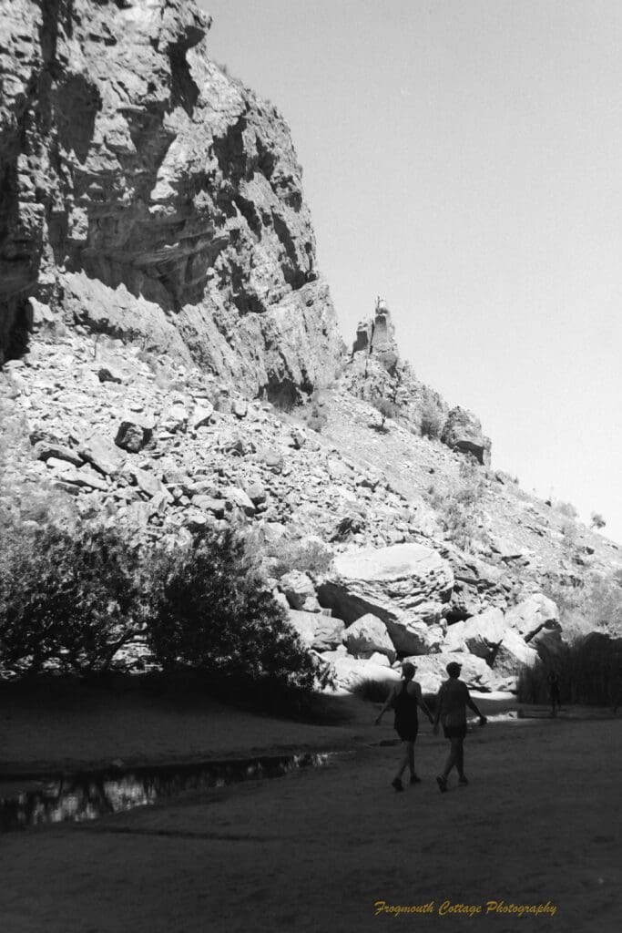 Black and white photo of two women walk beside a shallow stream of water at the bottom of a large gorge.