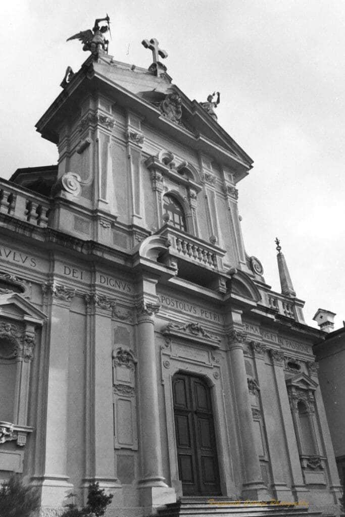 Black and white photograph of a formal stone building with a cross at the top and armed angels either side.