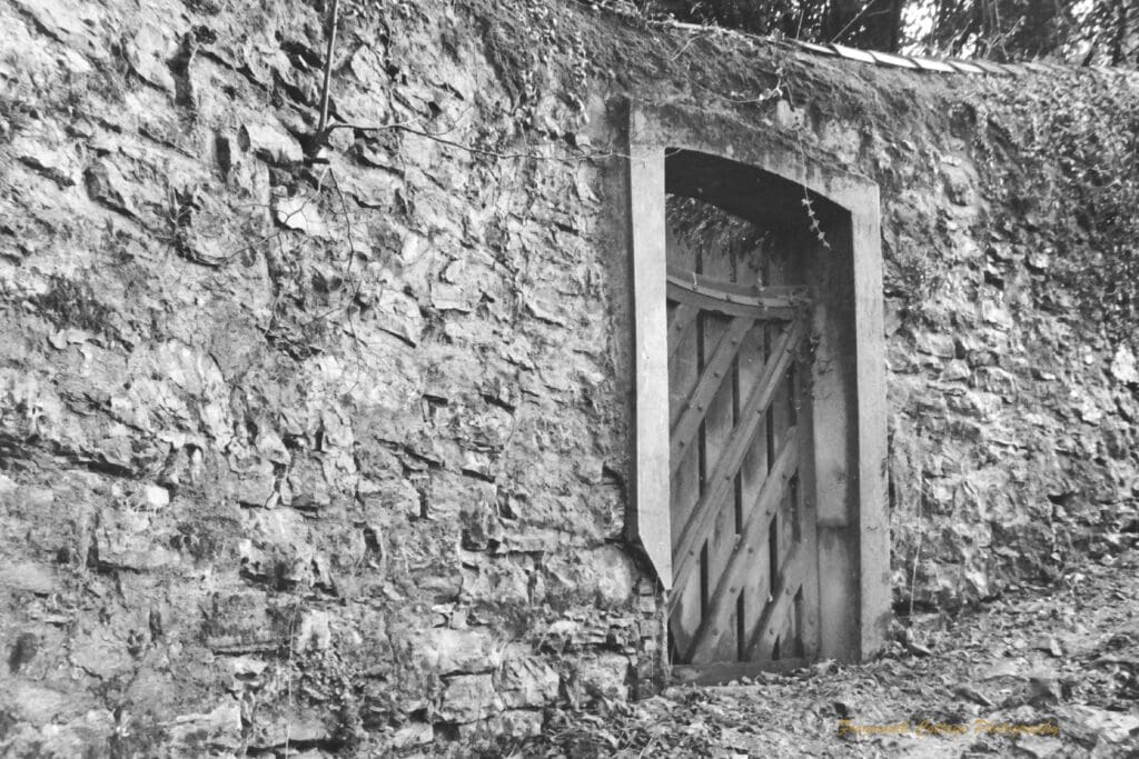 Black and white photograph of a wooden door set into a stone wall.
