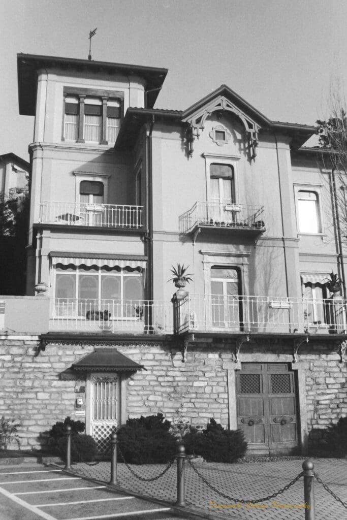 Black and white photograph of a stone house with two front doors, one metal one wooden, with three stories of windows and balconies above.
